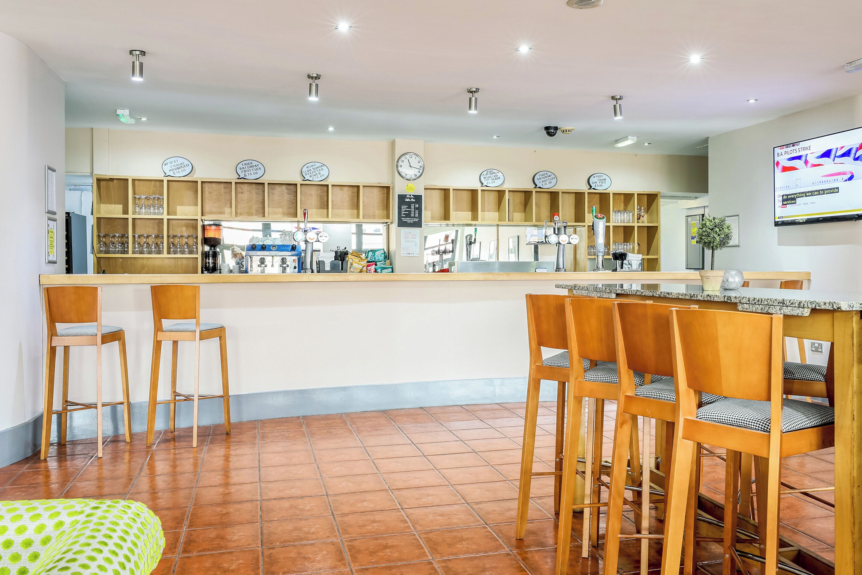 Una cafetería con mostrador, sillas de madera y piso de baldosas.