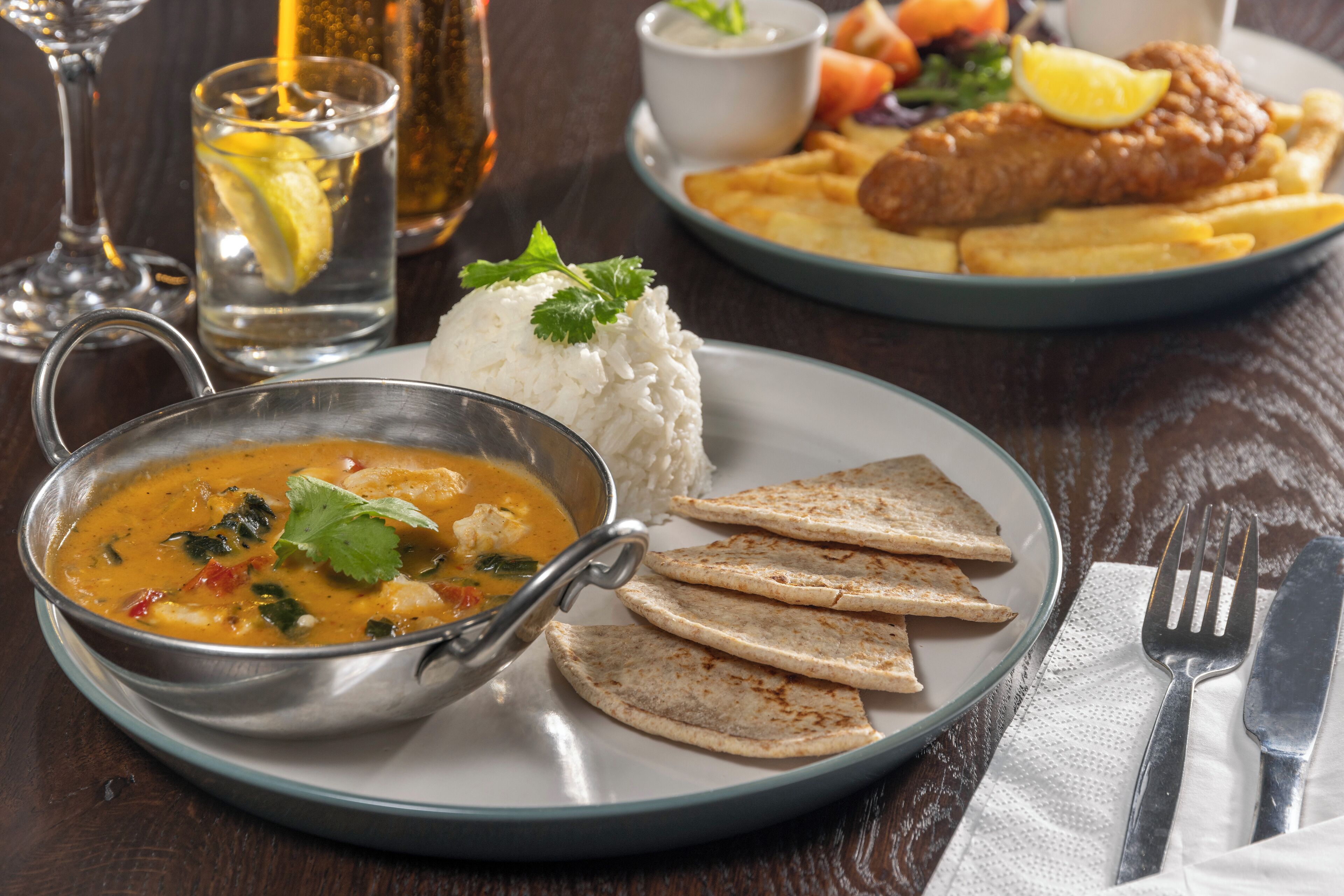 A meal consisting of rice, soup, flatbread, fish, fries, and a drink.
