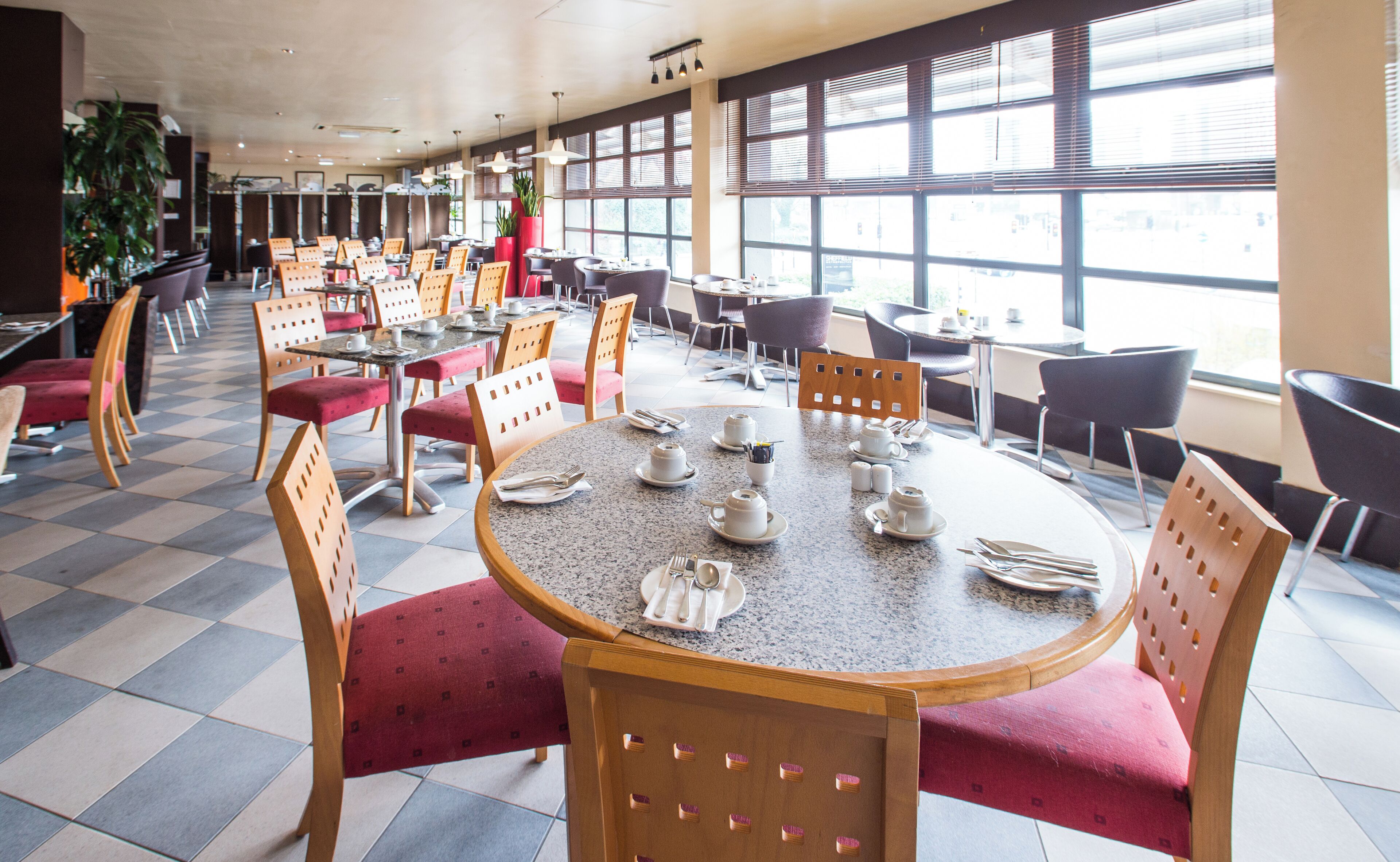 A spacious restaurant with high ceilings and large windows, featuring a mix of round and rectangular tables with chairs.