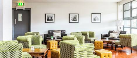 A lobby with green patterned chairs, a black sofa, and a wooden coffee table.