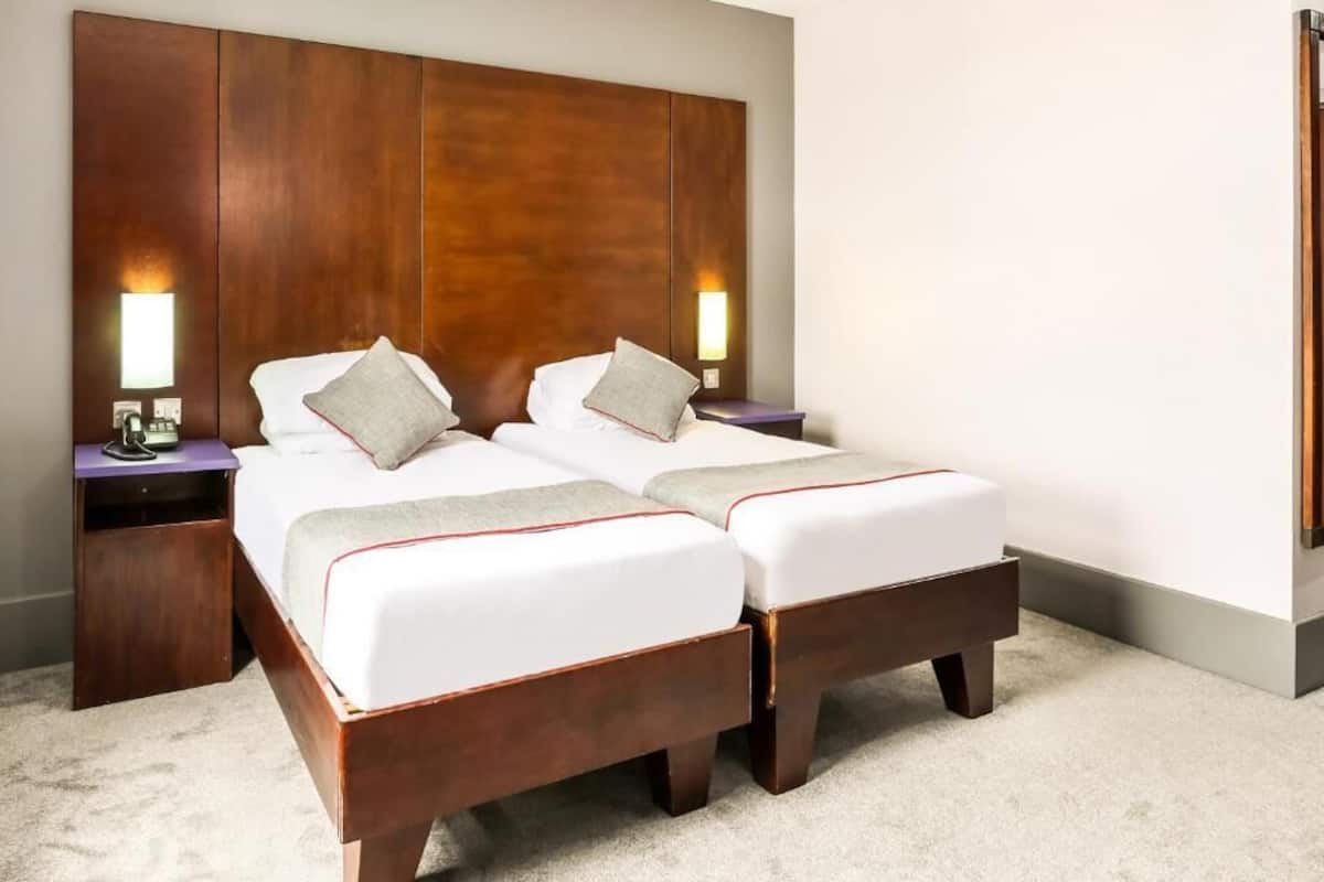 Una cama doble con cabecera de madera, dos mesitas de noche con lámparas y suelo cubierto de alfombra.