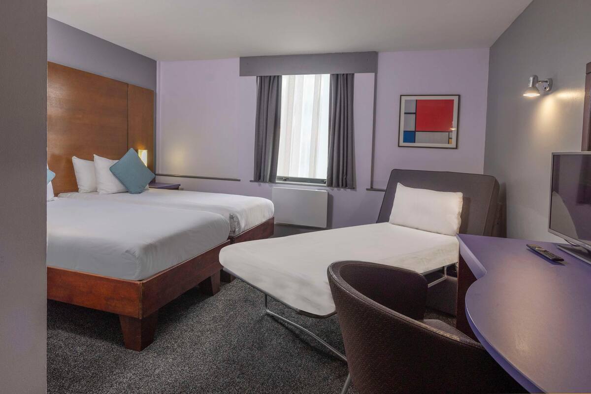 Habitación de hotel con dos camas, un escritorio, una silla, un televisor y una ventana con cortinas.