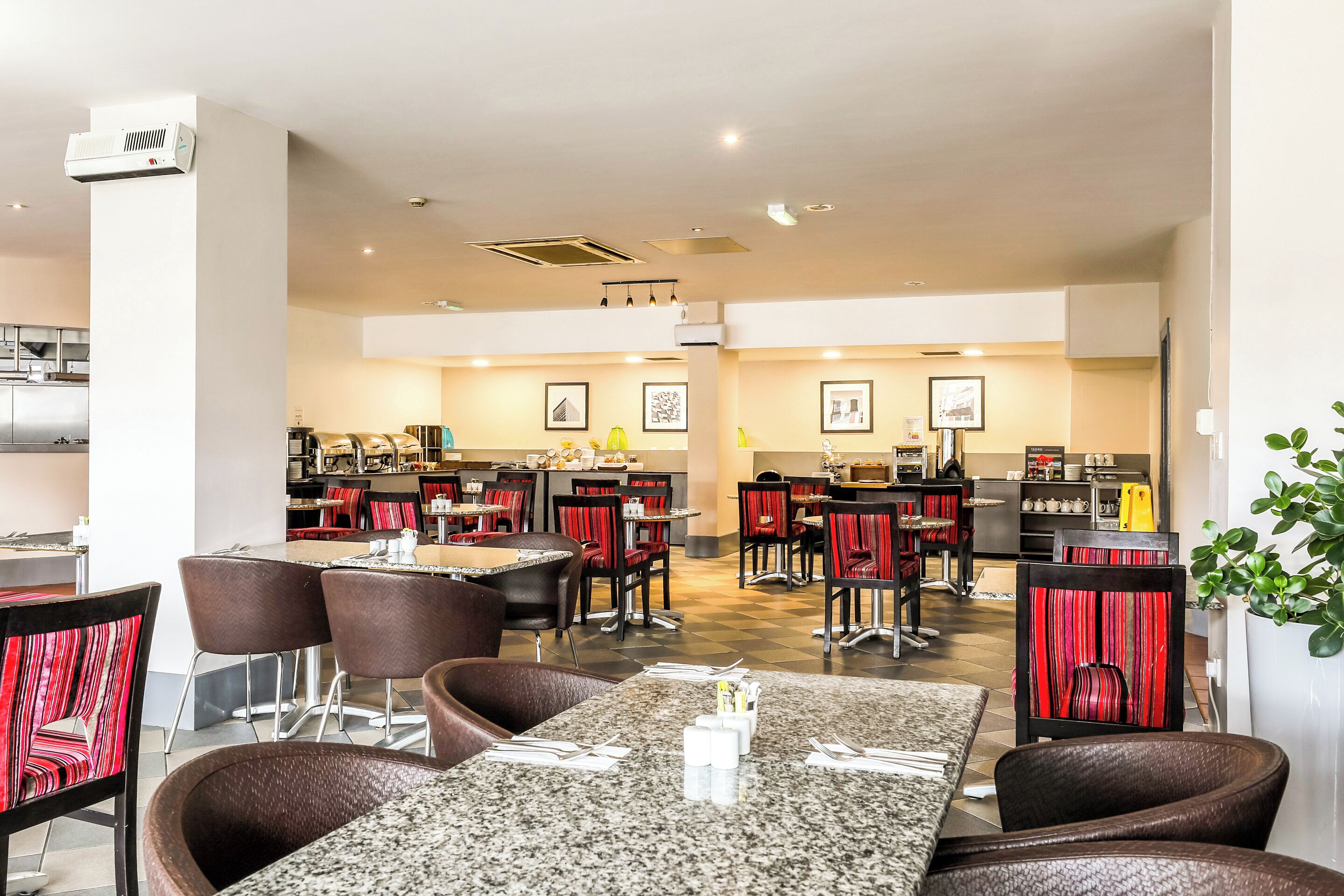 Un ristorante con diversi tavoli e sedie, un'area cucina e quadri appesi alle pareti.