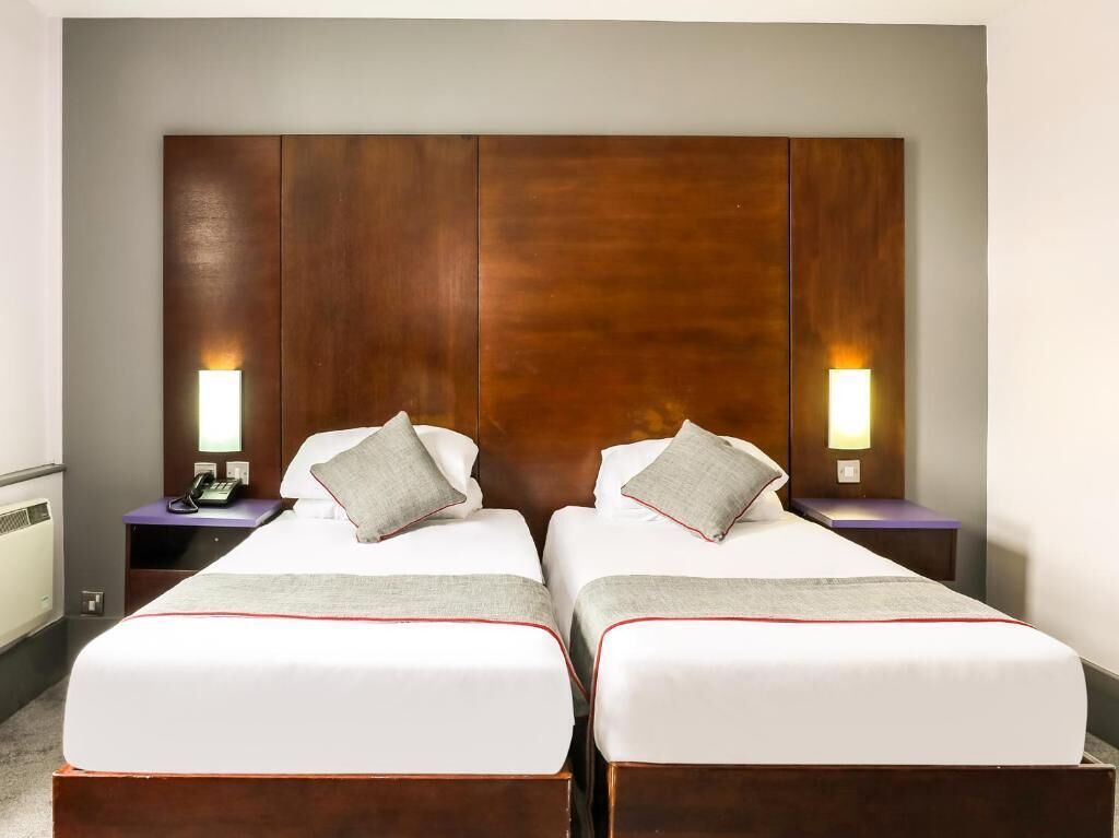 Habitación de hotel con dos camas, cabecero de madera, lámparas de noche y un teléfono en la mesita.