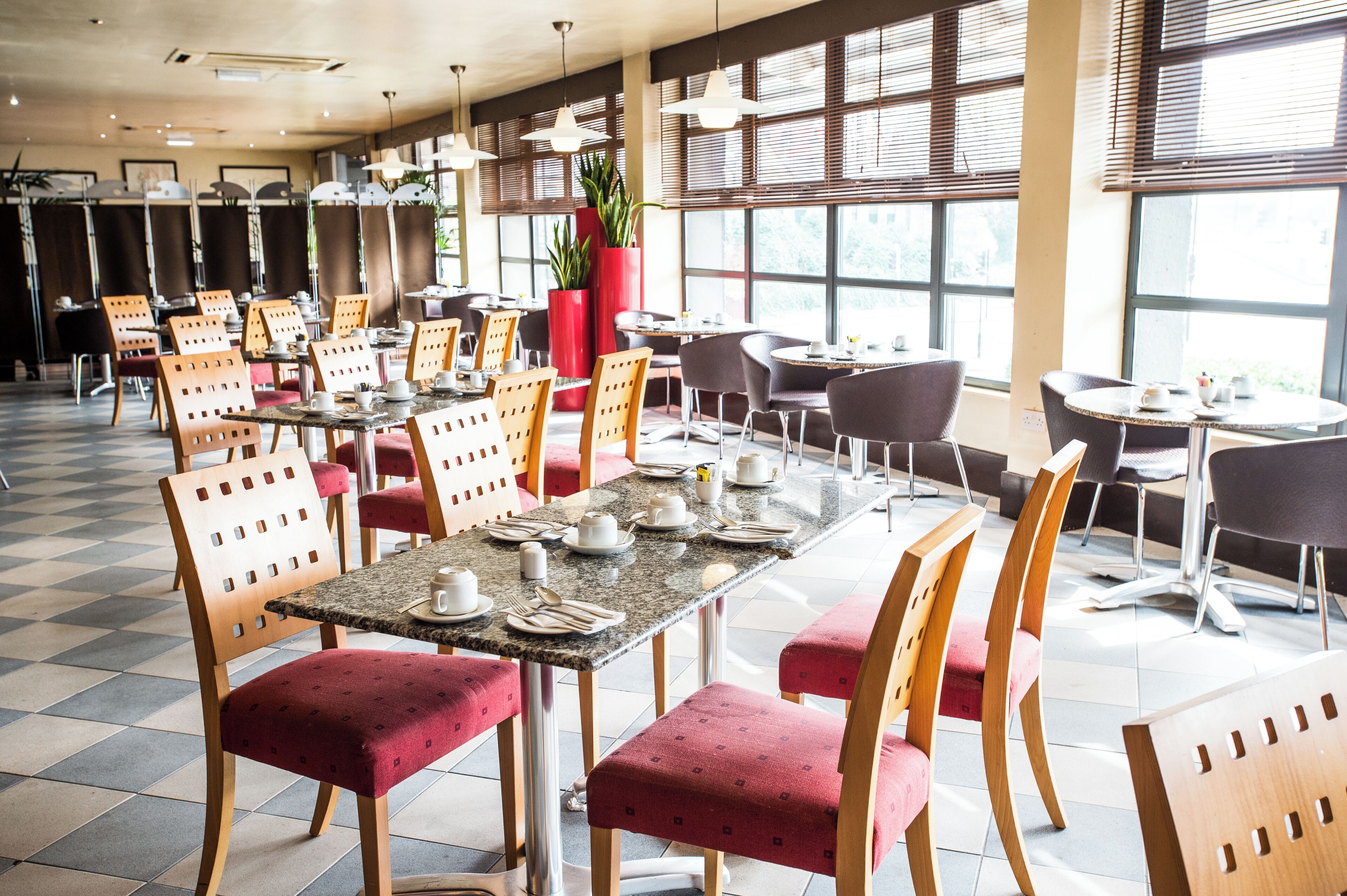 A spacious dining area with multiple tables and chairs, large windows, and potted plants.