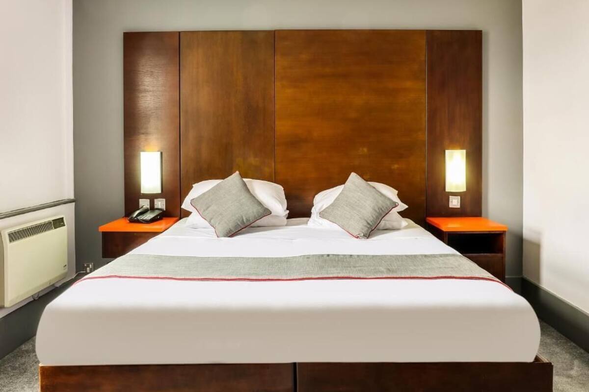 Habitación de hotel con una cama grande, cabecero de madera, dos mesitas de noche con lámparas y un teléfono.