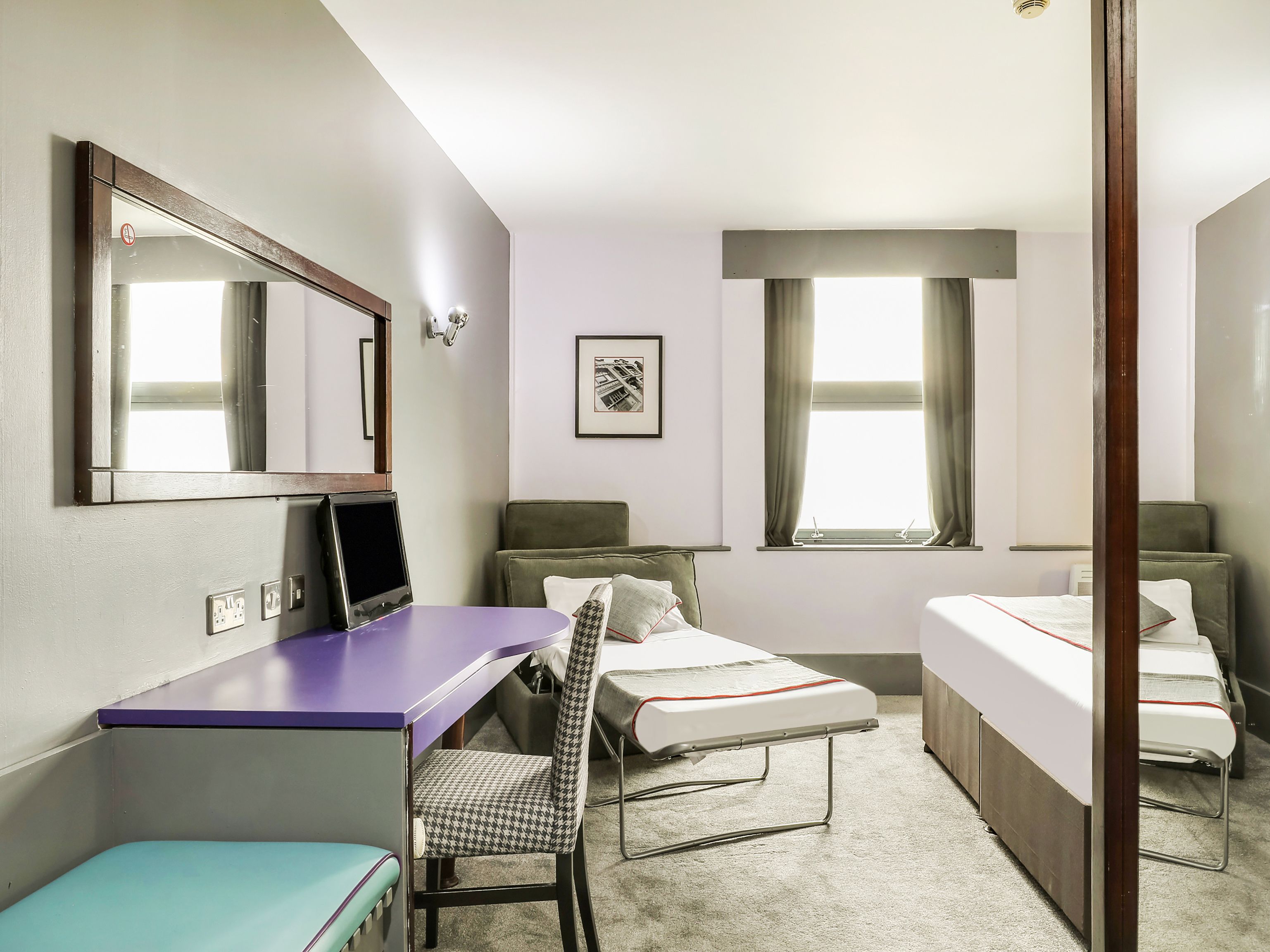 Un dormitorio con un escritorio, dos camas, una silla y una ventana.