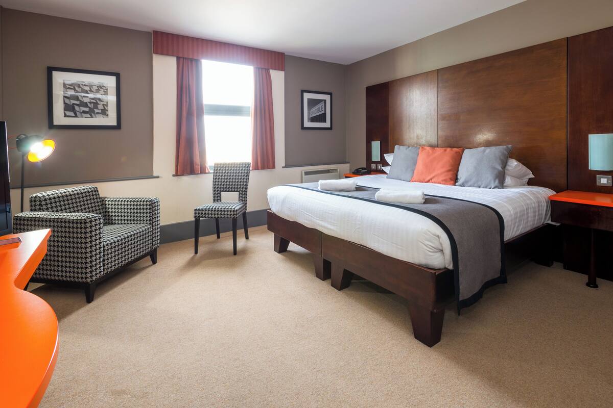 Una habitación de hotel con una cama grande, dos sillas, un escritorio y una lámpara.
