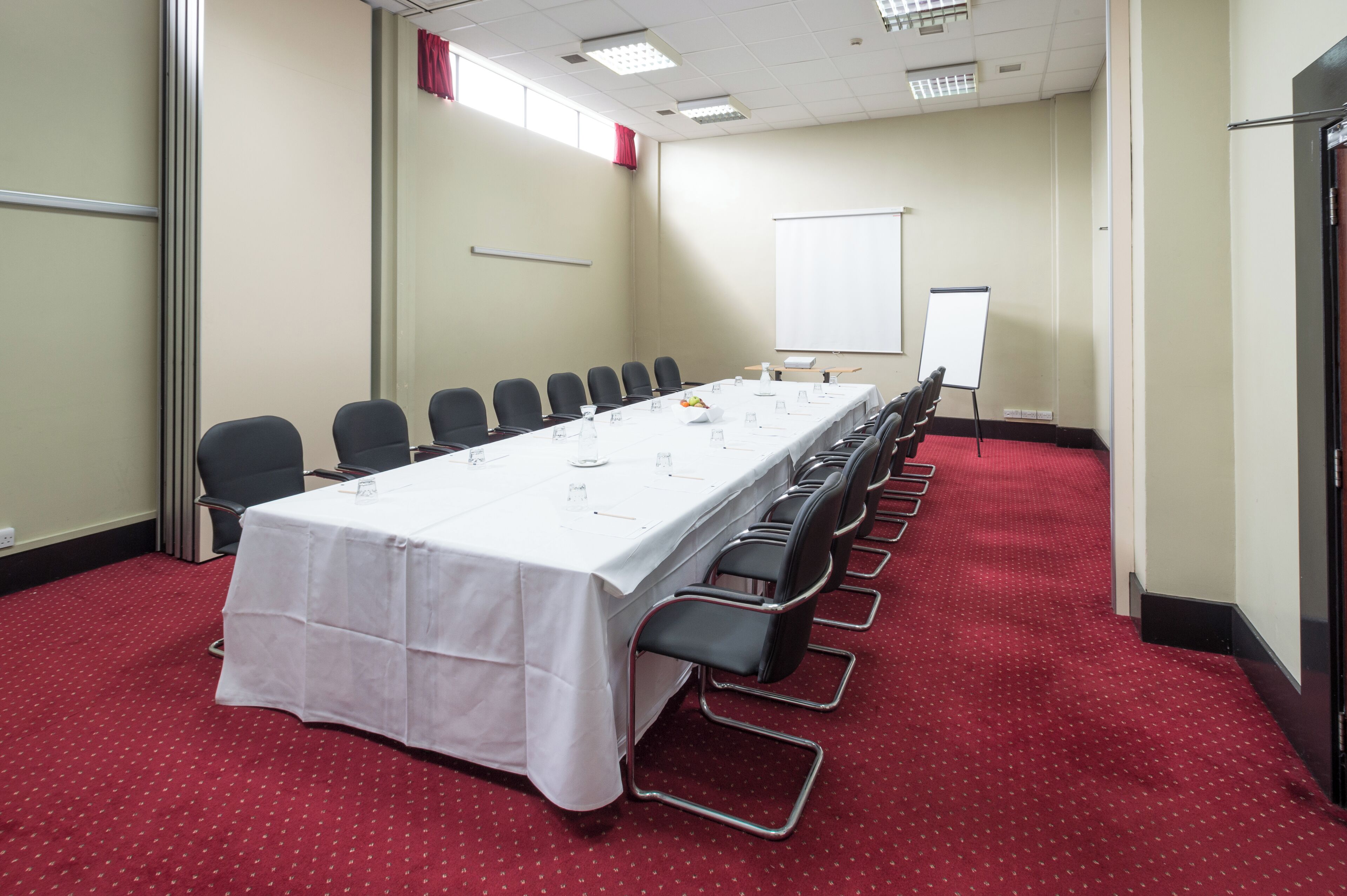 A conference room with a long table, chairs, a whiteboard, and a red carpeted floor.