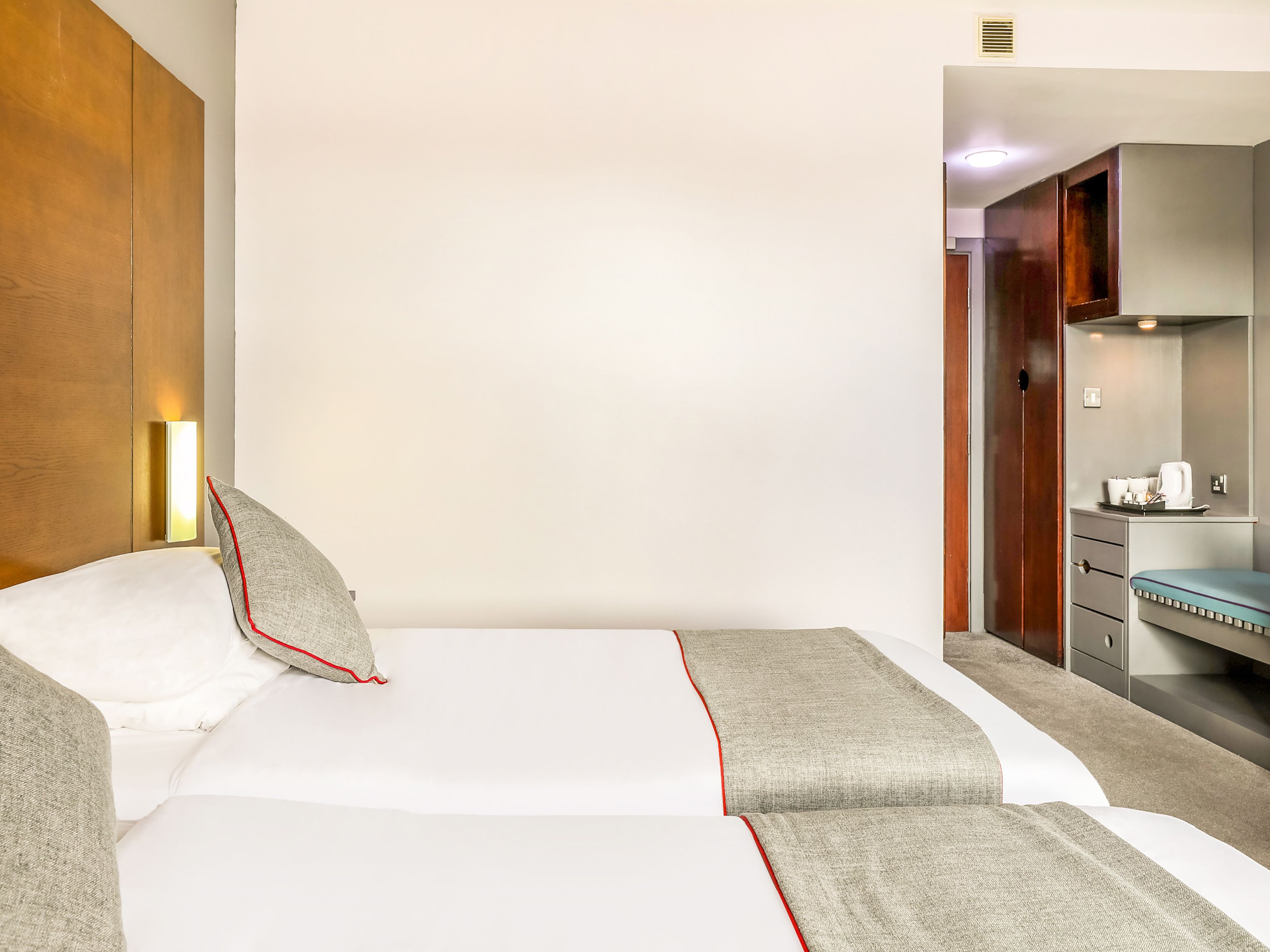 A hotel room with a bed, a bedside table, a mirror, and a kitchenette.