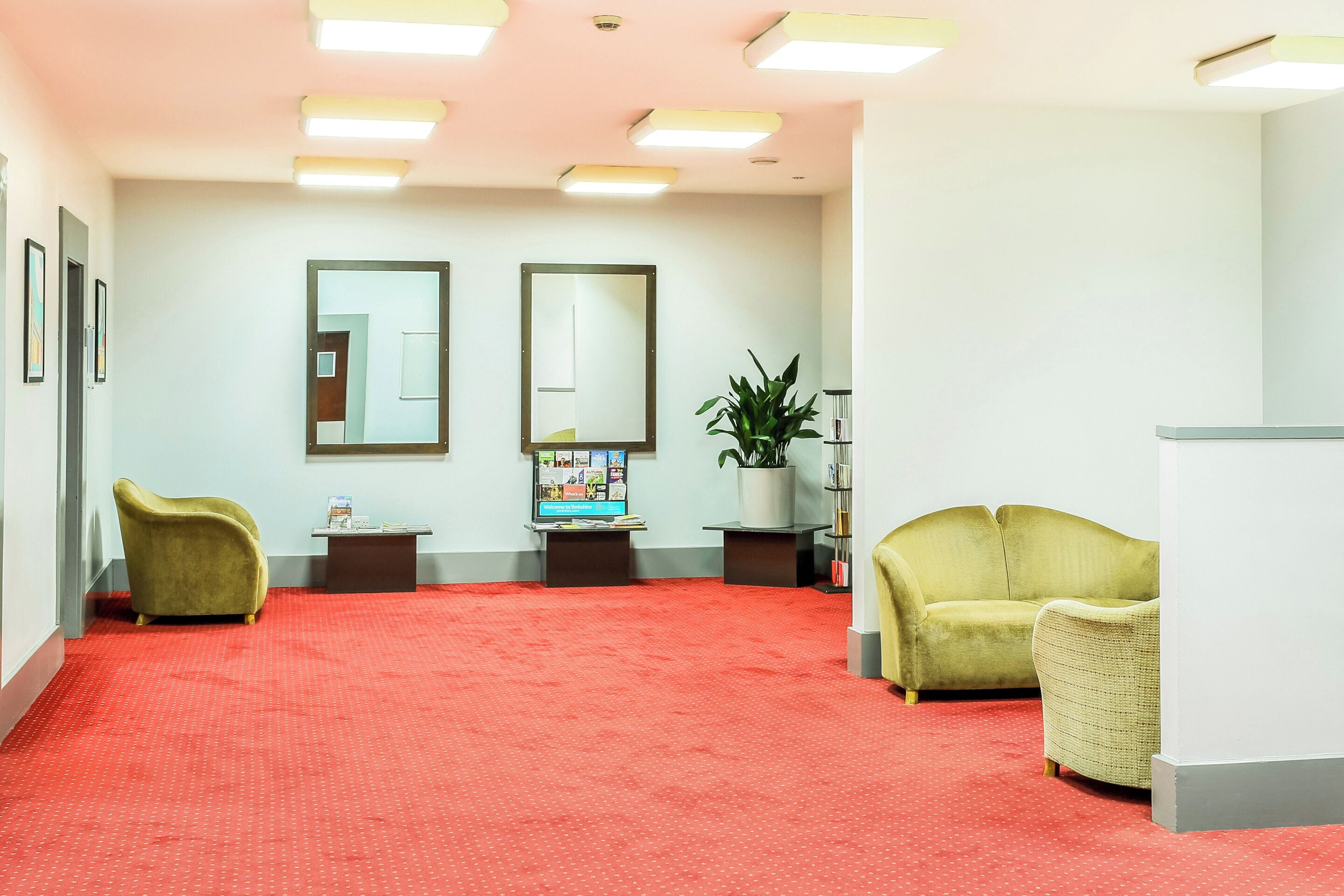 Een receptiezone met een rode loper, twee fauteuils, een bijzettafeltje met een plant en twee spiegels aan de muur.