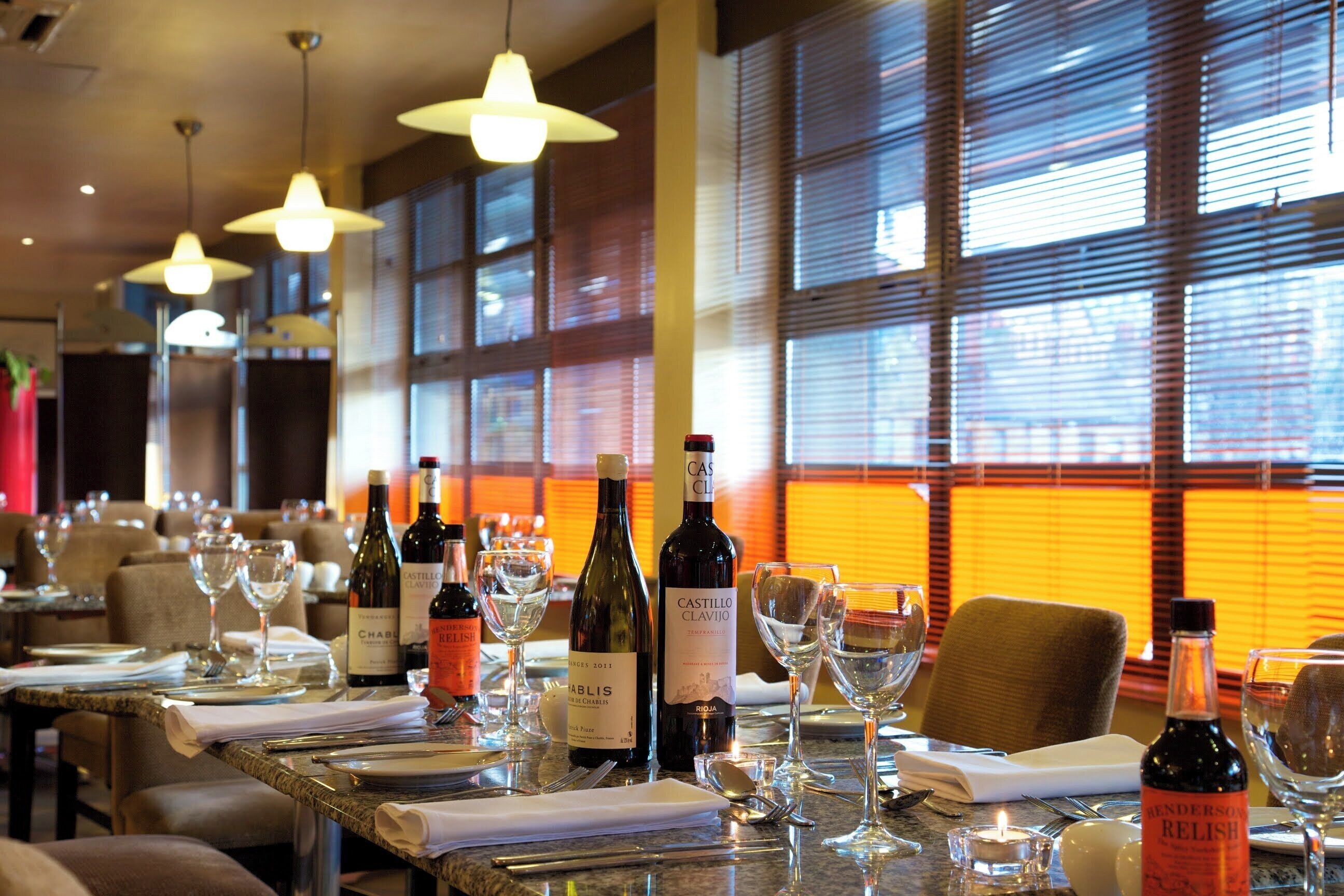 L’intérieur d’un restaurant, avec des tables dressées pour le service, des bouteilles de vin et des verres.
