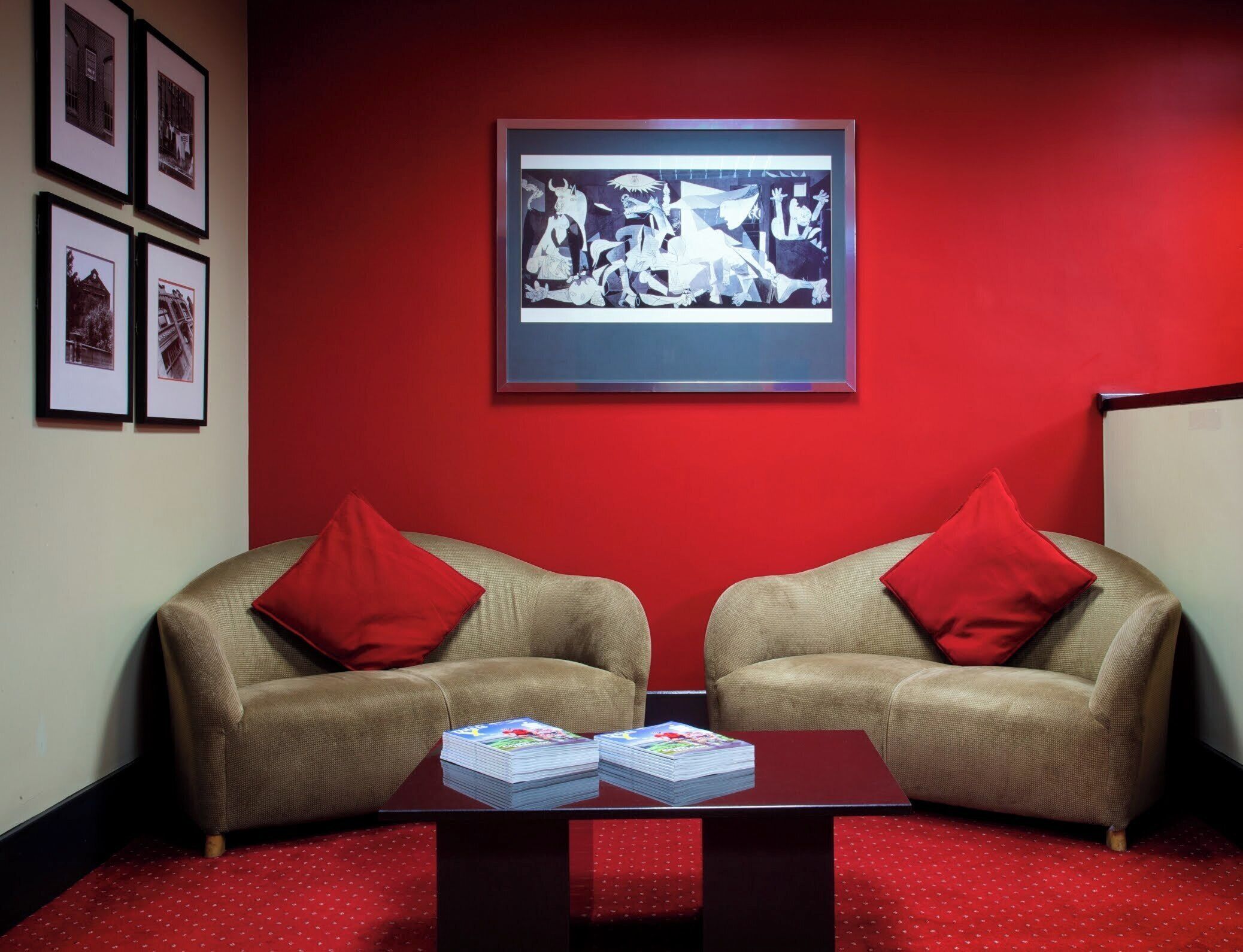 Una habitación con dos sofás beige con cojines rojos, una alfombra roja y una obra de arte enmarcada en la pared.