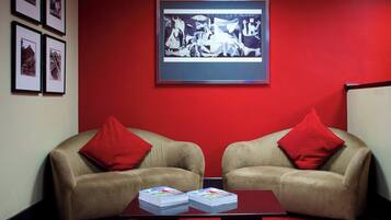 Una habitación con dos sofás beige con cojines rojos, una alfombra roja y una obra de arte enmarcada en la pared.