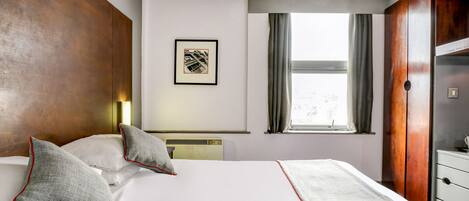 A hotel room with a large bed, a framed picture on the wall, a window with curtains, and a wooden wardrobe.