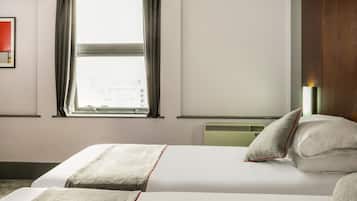 Habitación de hotel con dos camas, una ventana con cortinas, una lámpara de pared y un radiador.