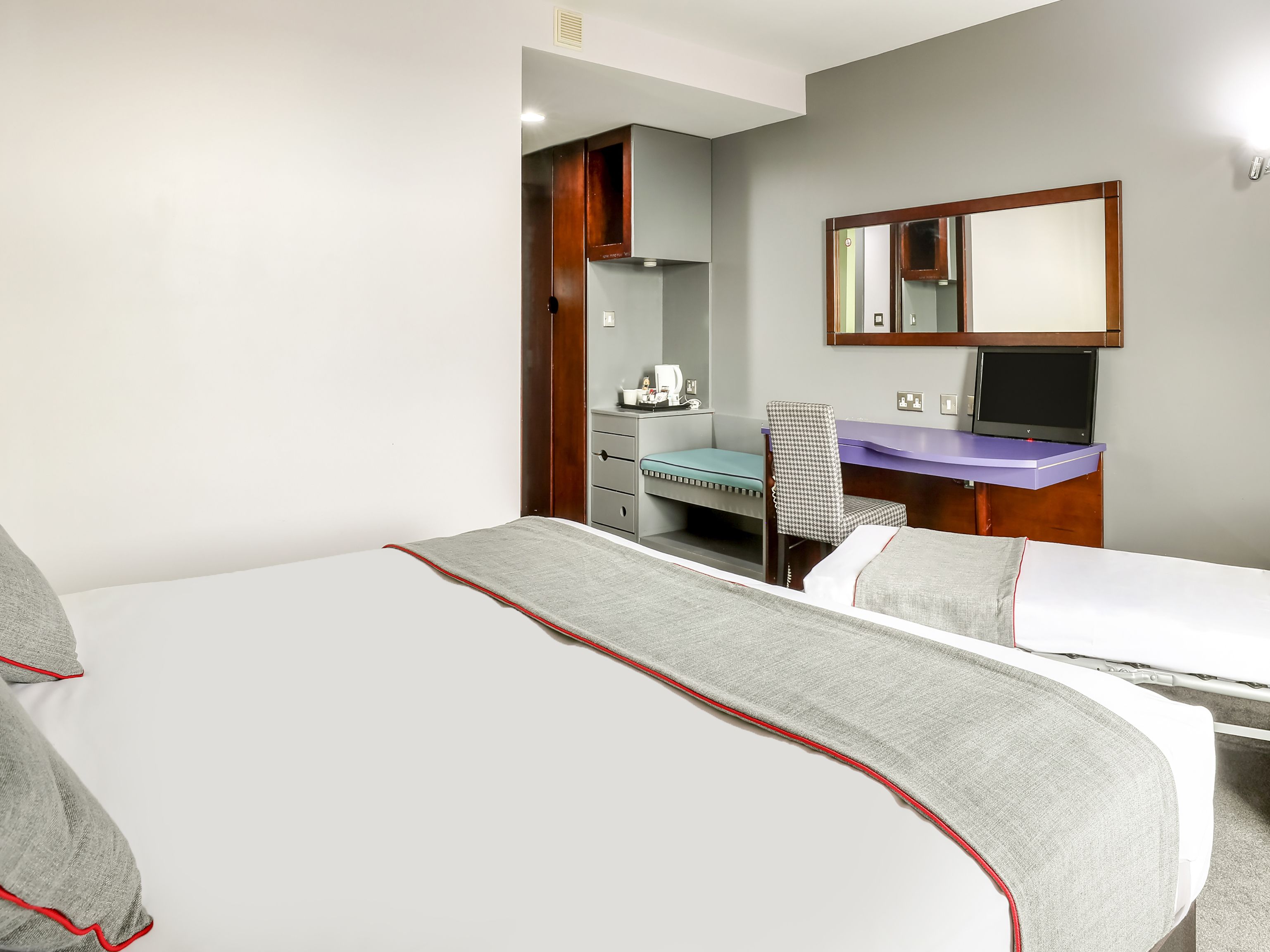 Una habitación de hotel con cama, escritorio, silla, espejo y una mesita.