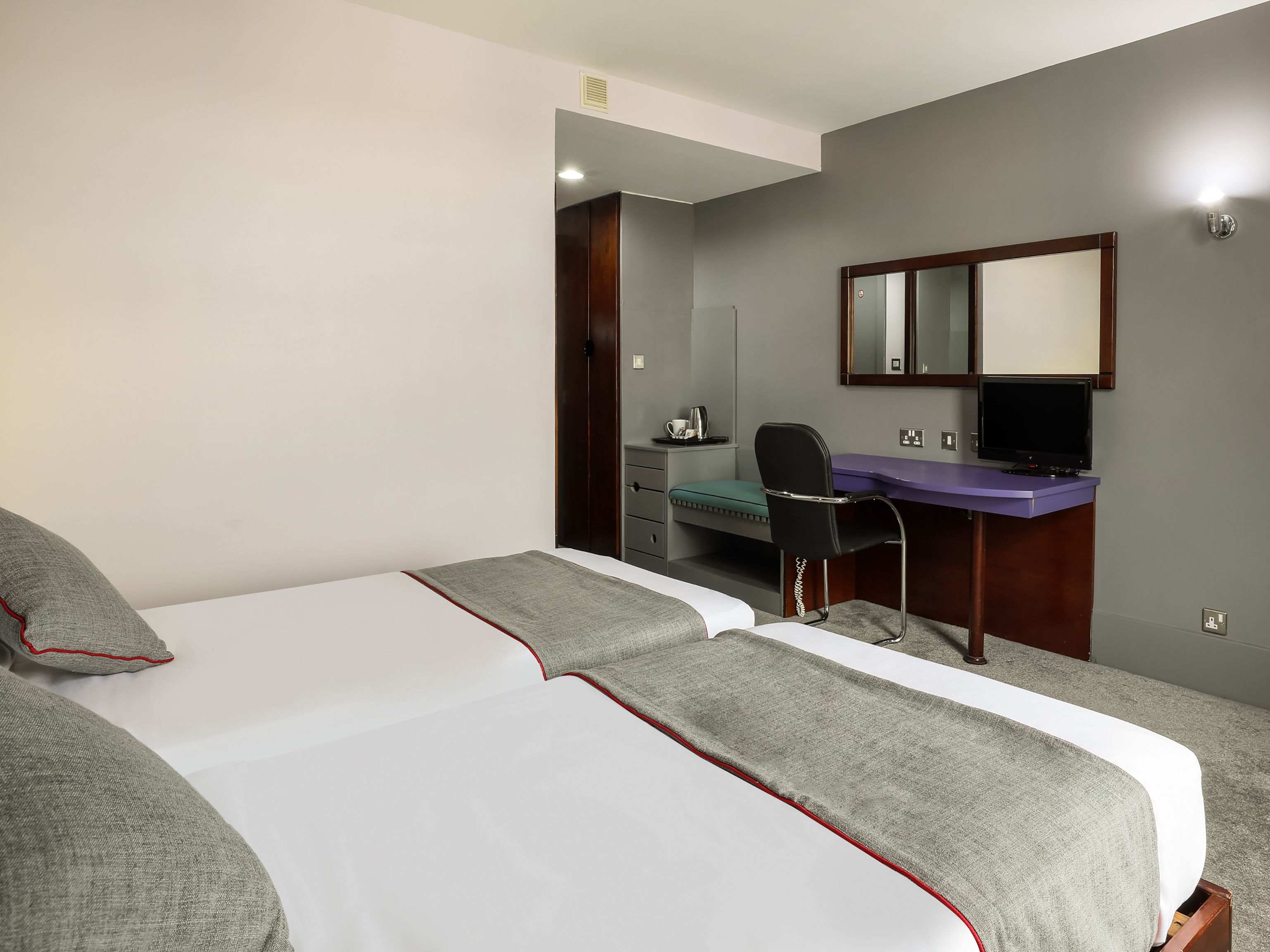 A hotel room with a bed, a desk, a chair, and a mirror.