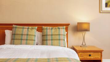 Una cama bien hecha con ropa de cama escocesa, un cabecero de madera y una mesita de noche con una lámpara.