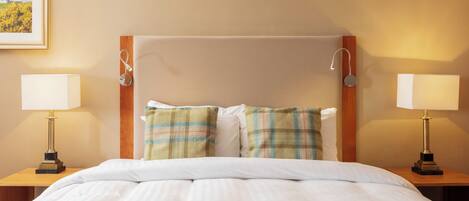 A hotel room with a bed, two bedside tables, two lamps, a headboard, and a framed picture on the wall.