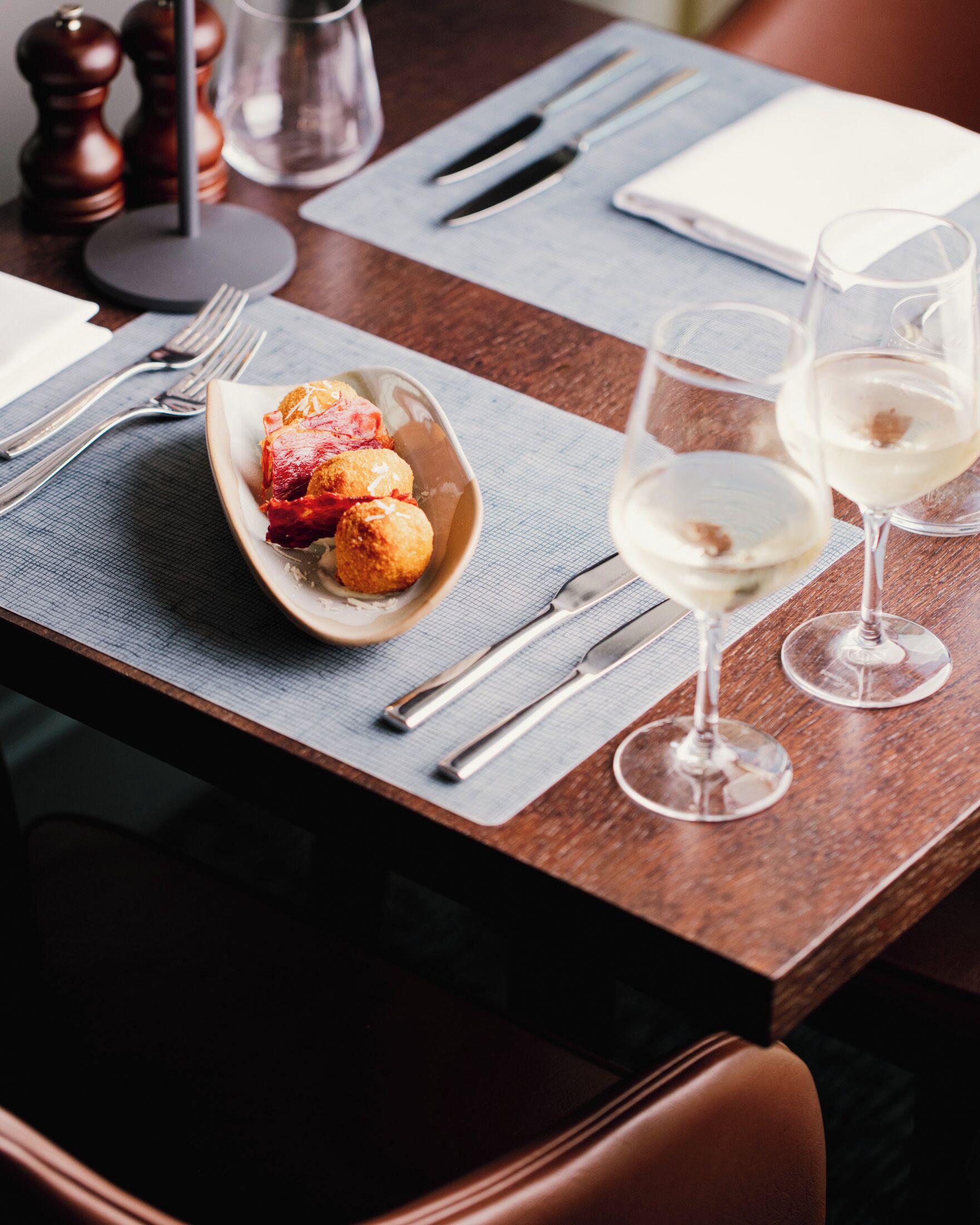 Una mesa de comedor dispuesta con un plato de comida, copas de vino, cubiertos y una servilleta.