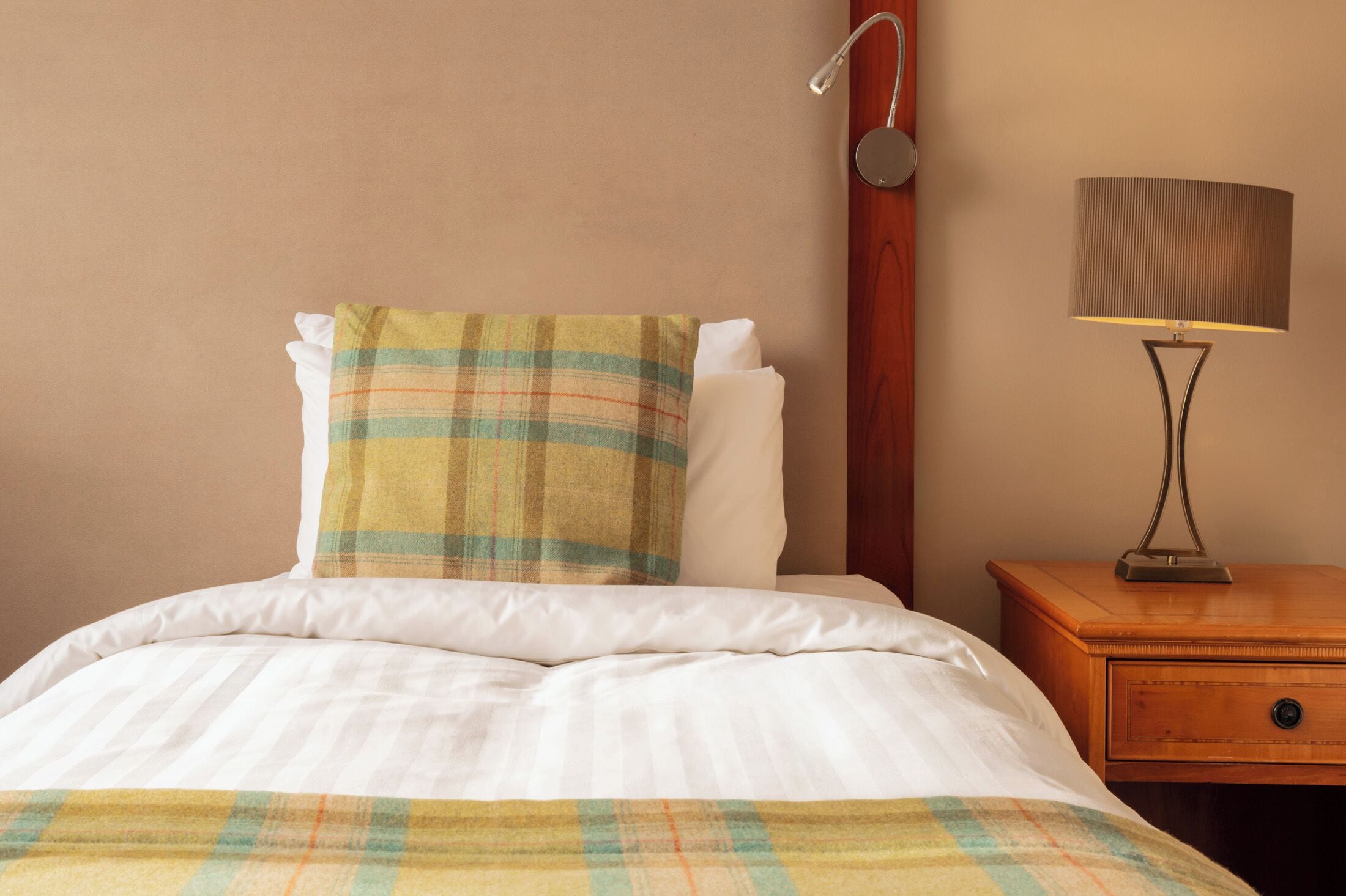 A neatly made bed with a plaid blanket, a bedside lamp, and a wooden nightstand.