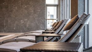 A row of sun loungers with cushions, arranged in a modern indoor setting with a stone wall and large windows. - Carnoustie Golf Hotel (Carnoustie)