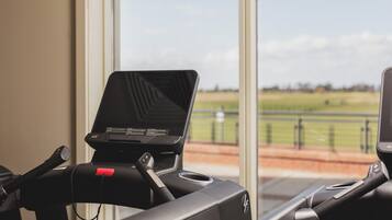 A treadmill with a digital display, positioned near a window with a view of a green field and a fence.