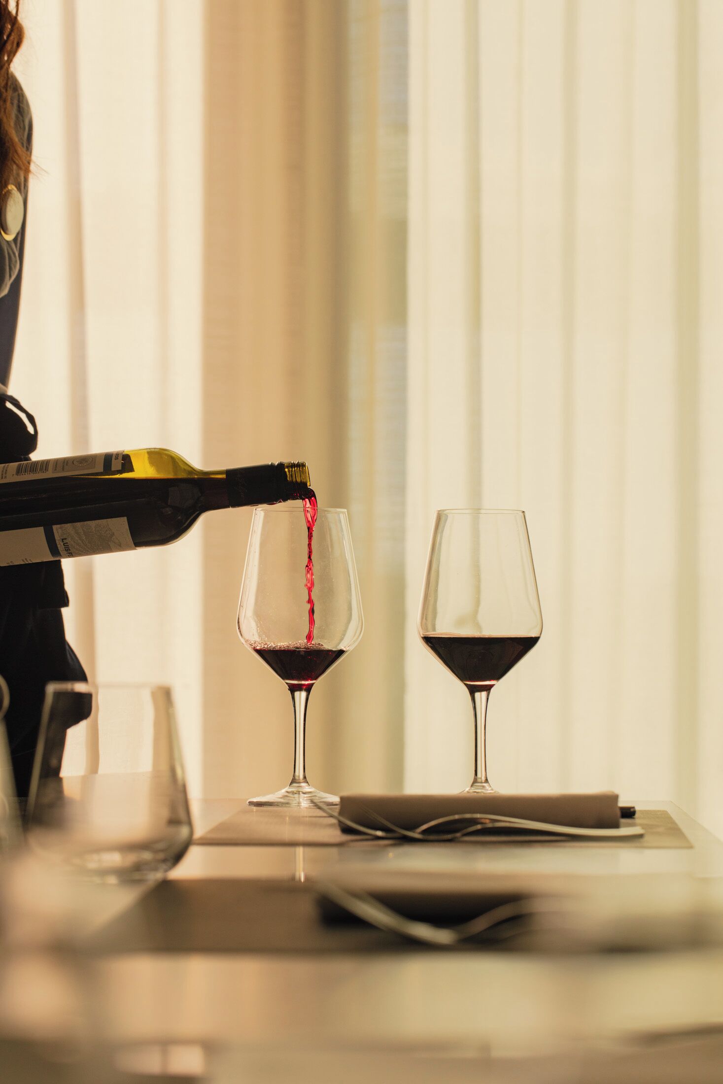 Una botella de vino vertiendo vino en una copa sobre una mesa, con otra copa y un libro.