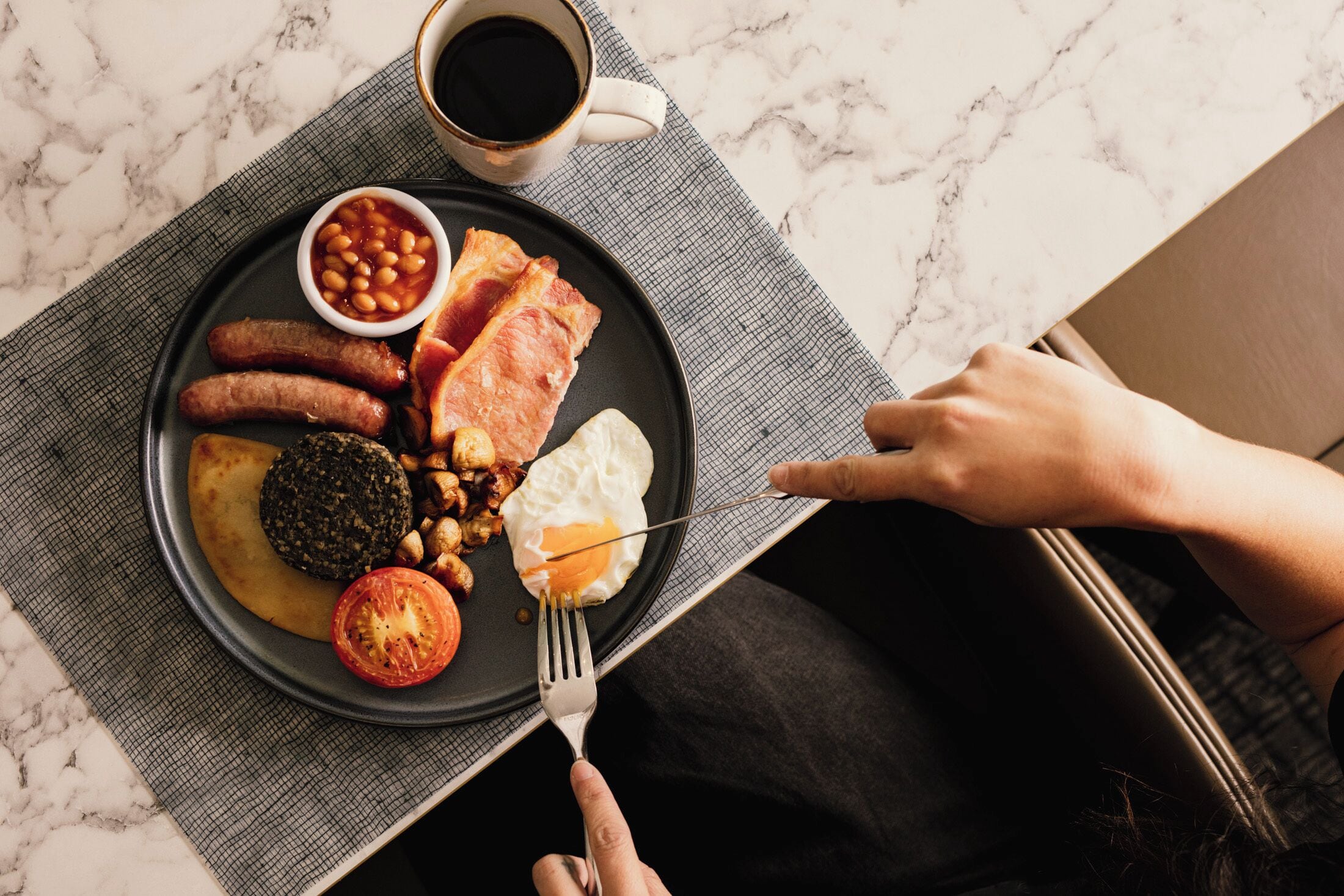 A breakfast plate with sausages, bacon, eggs, beans, and a tomato on a marble countertop.