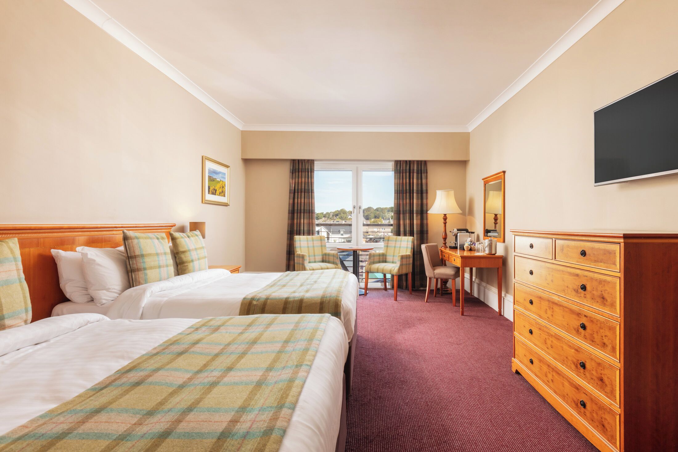 A hotel room with two beds, a desk, a chair, a dresser, and a TV.