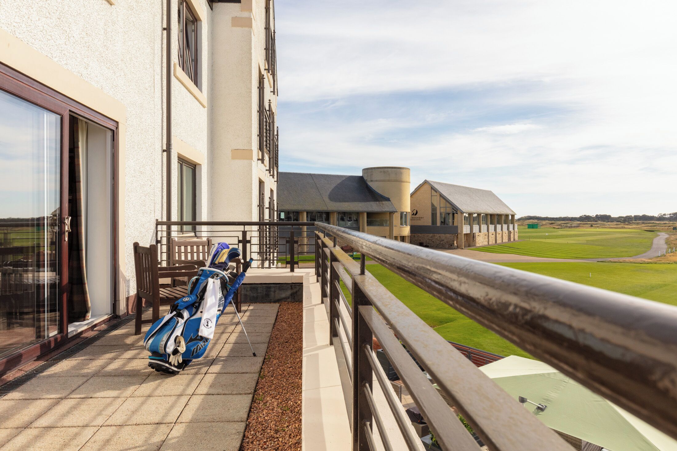 Ein Balkon mit Golftaschen, ein Gebäude mit einer gewölbten Dachlinie und Blick auf einen Golfplatz.