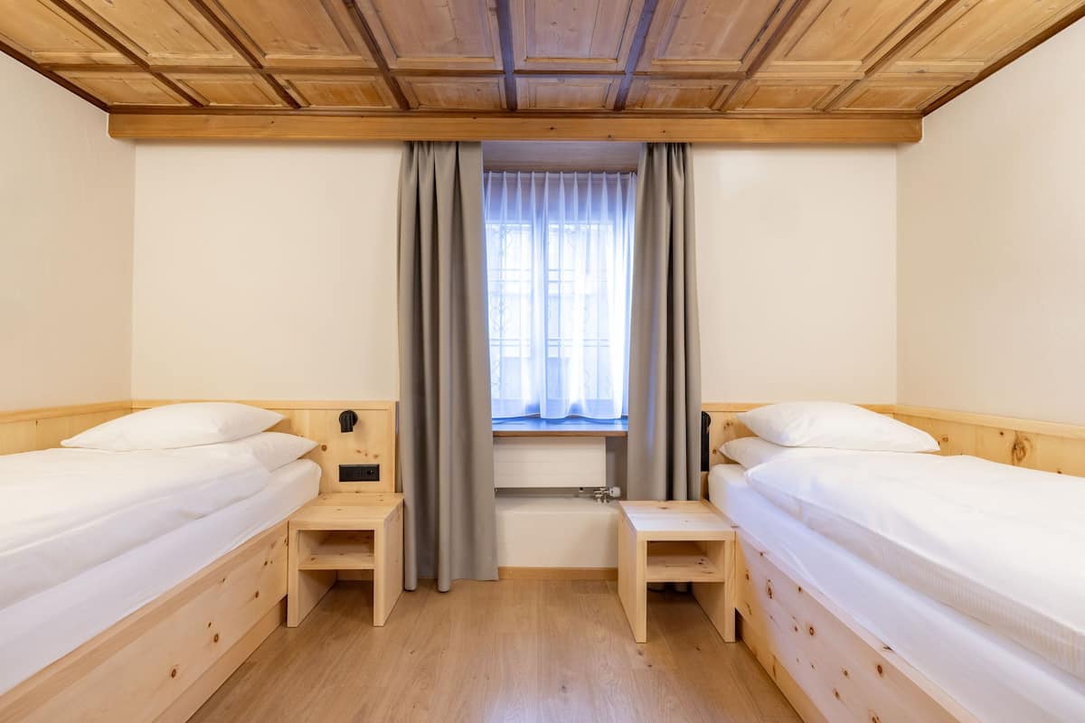 Una habitación con dos camas de madera, una ventana con cortinas y techo de madera.