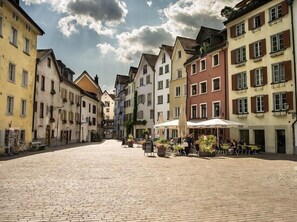 A cobblestone street lined with colorful buildings, a central open space with tables and chairs, and a few people. - Hotel Stern Chur (Chur)