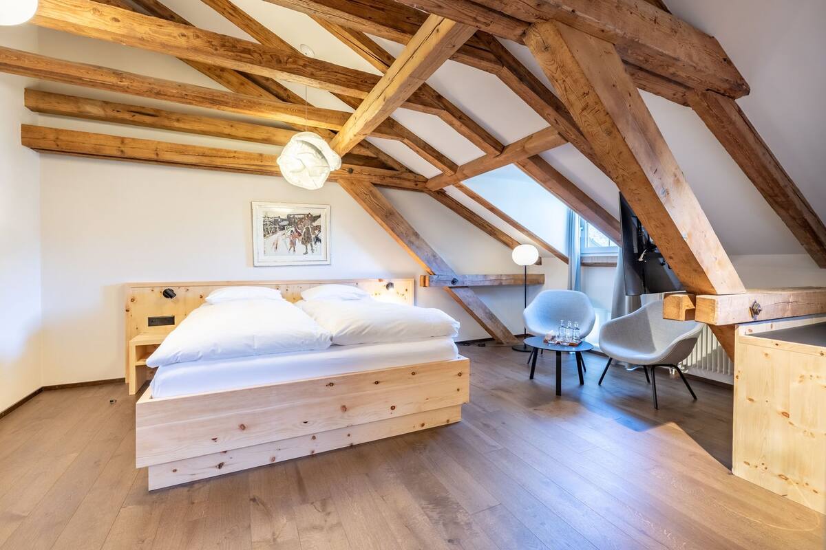Un dormitorio con techo de madera, una cama, una silla y una mesa.