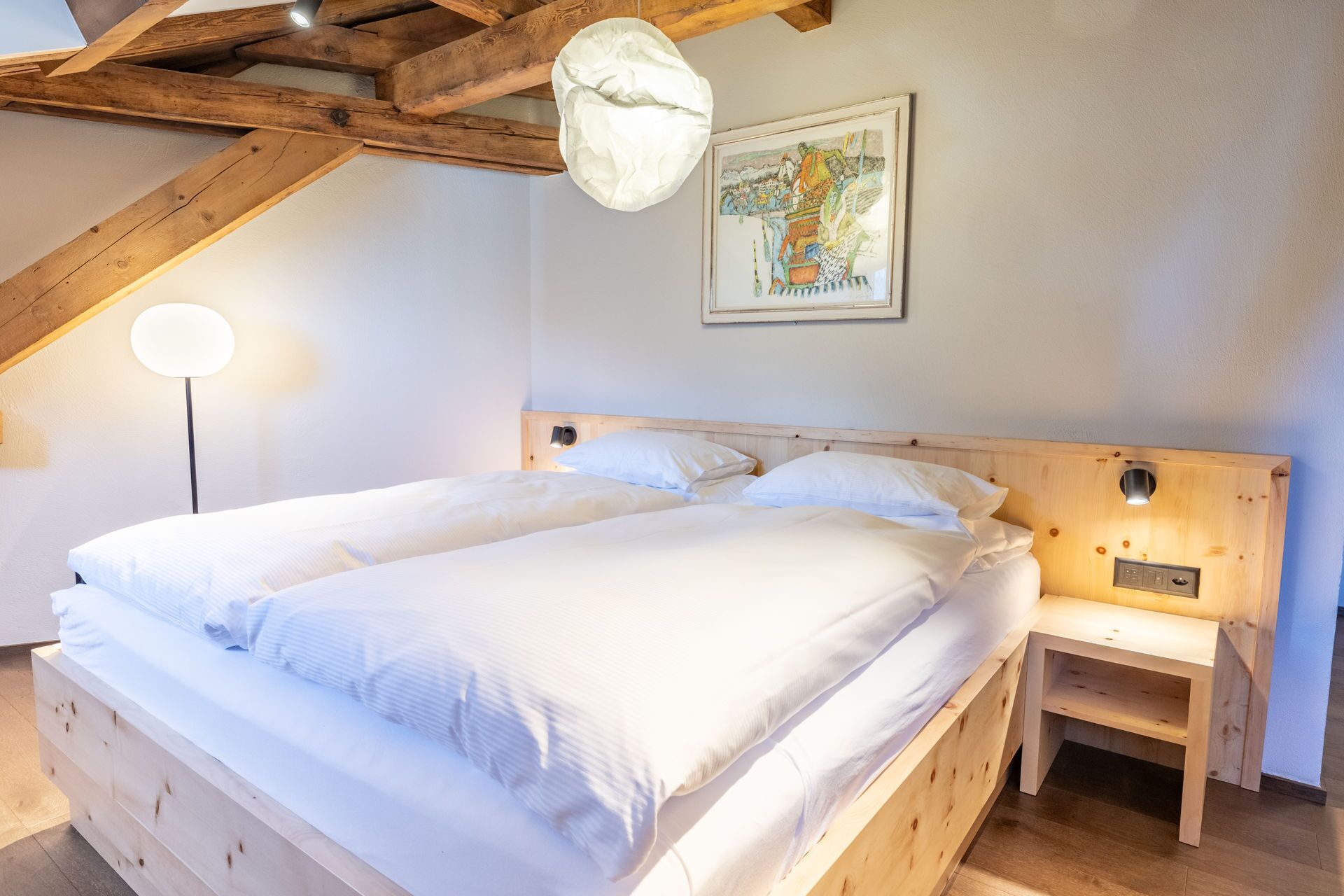 Un dormitorio con cama de madera, una mesita de noche, una lámpara de pared y un cuadro enmarcado.