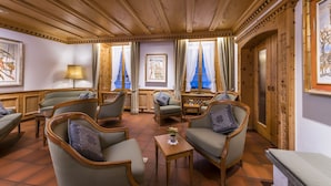A room with wooden paneling, a sofa, armchairs, a small table with a plant, and two windows with blue curtains. - Hotel Stern Chur (Chur)