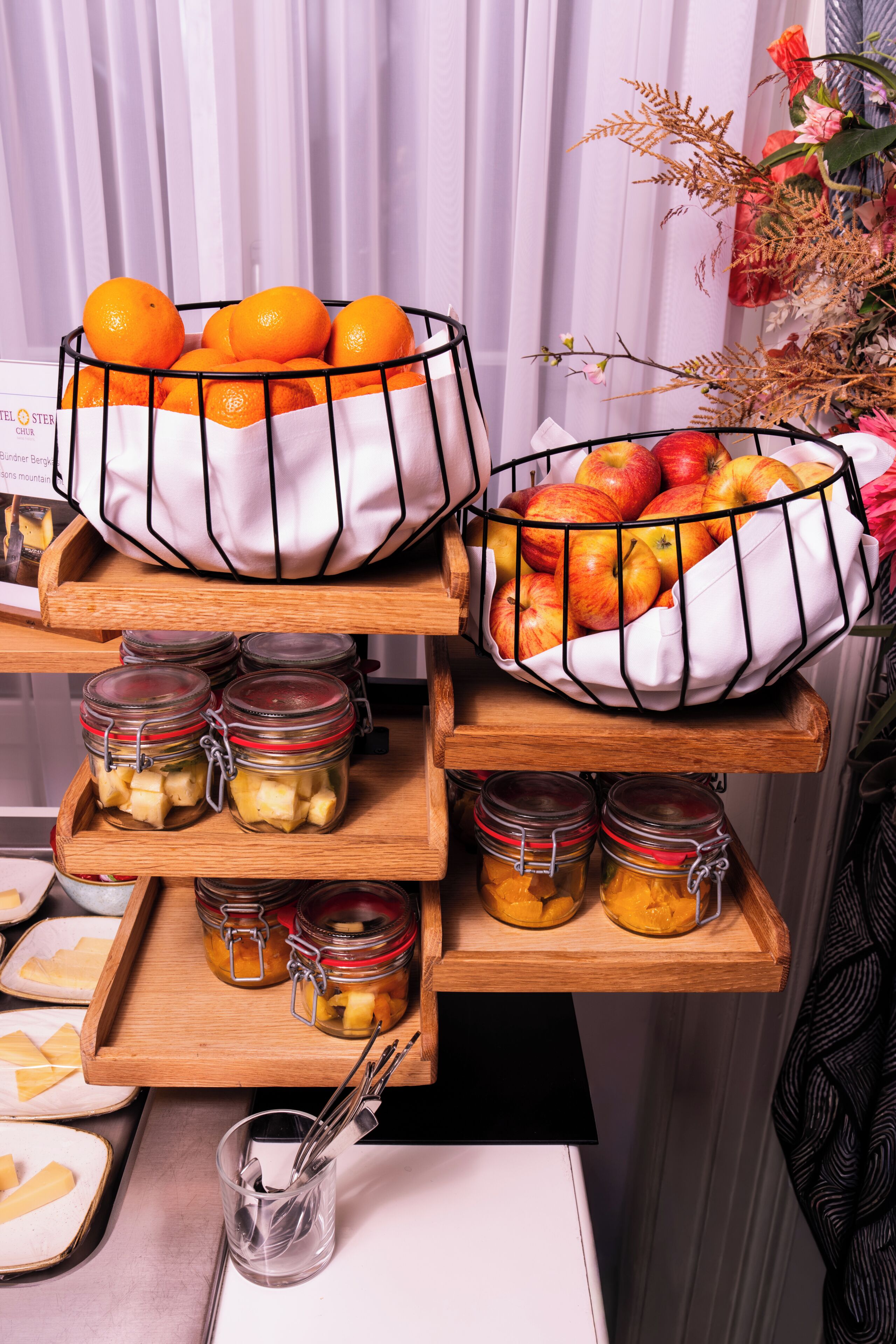 Un buffet de petit-déjeuner avec des saladiers de fruits, des pots de confitures et un présentoir contenant des couverts.