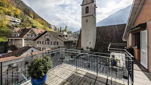 A balcony with a potted plant, a clock tower, and buildings with traditional architecture. - Hotel Stern Chur (Chur)