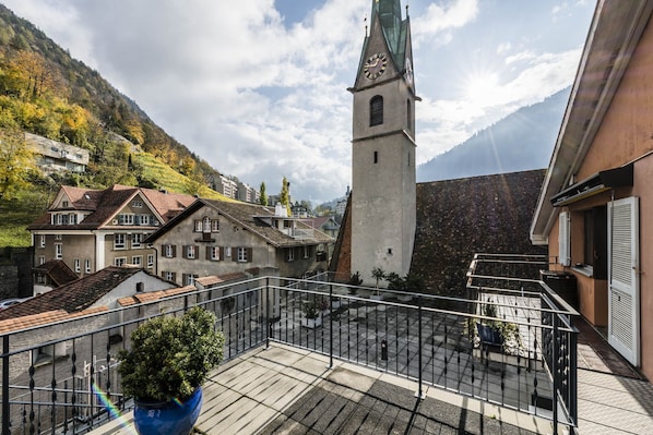 A balcony with a potted plant, a clock tower, and buildings with traditional architecture. - Hotel Stern Chur (Chur)