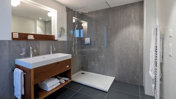Un baño moderno con ducha envuelta en vidrio, tocador con espejo y perchero.