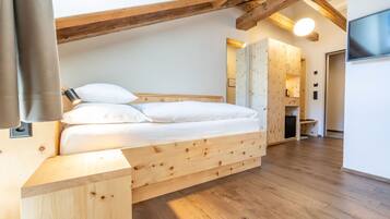 A wooden bed in a room with a sloped ceiling and a built-in wardrobe.