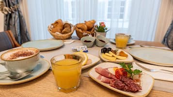 A breakfast table with croissants, cheese, tomatoes, and a glass of orange juice.