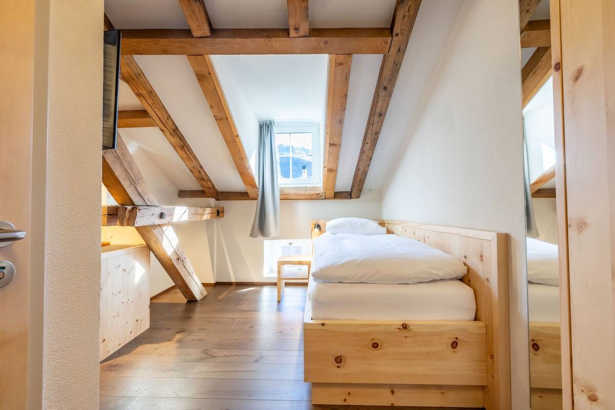 Un dormitorio con cama de madera, una mesita de noche pequeña y una ventana con vistas al exterior.