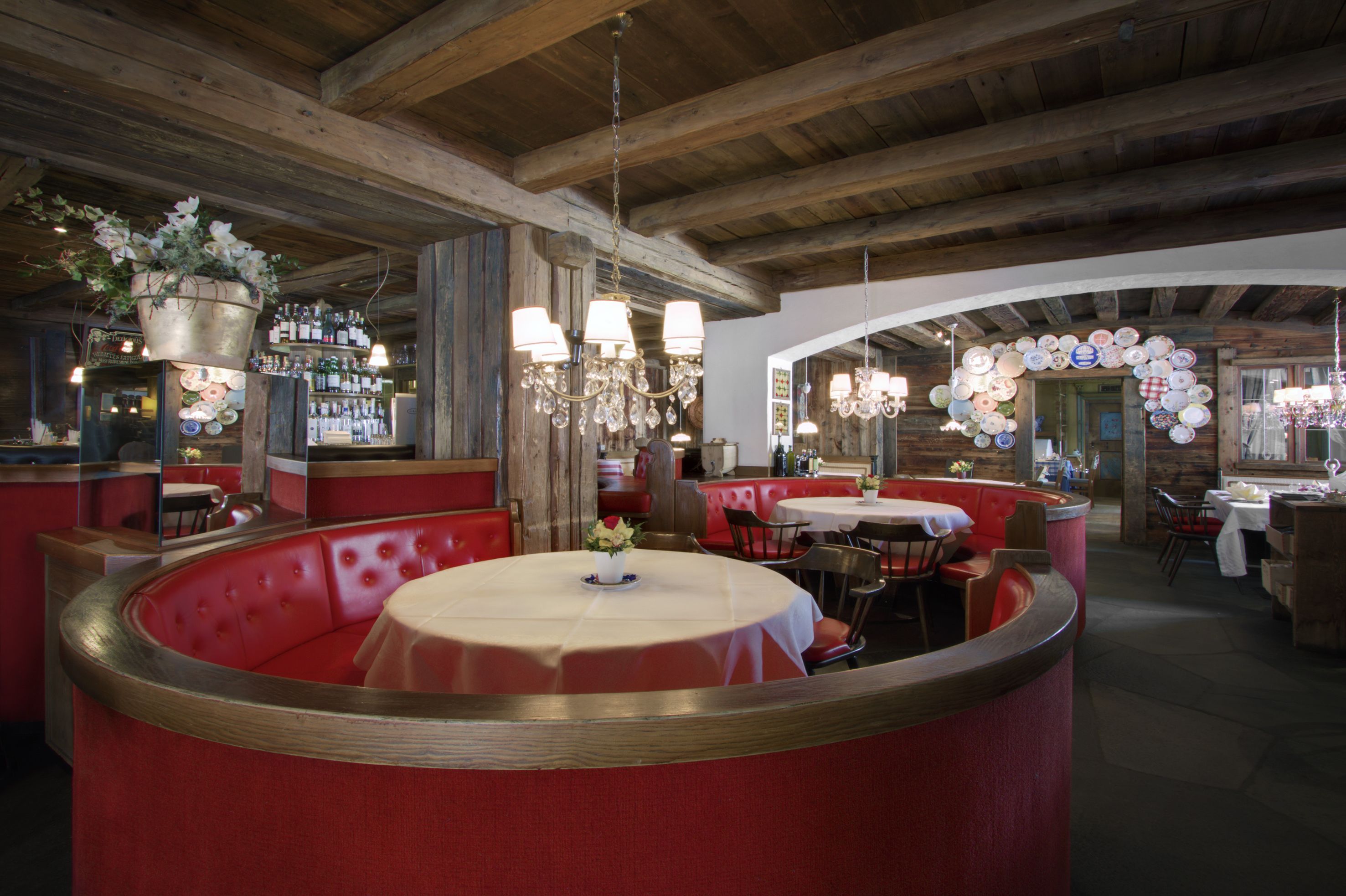 Un restaurant avec des banquettes rouges, un coin bar et un lustre.