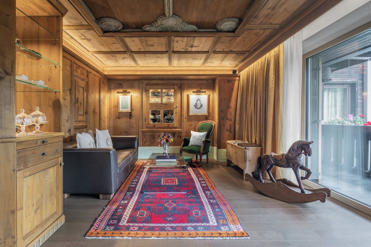 Een kamer met houten lambrisering, een bank, een schommelpaard en een groot raam.