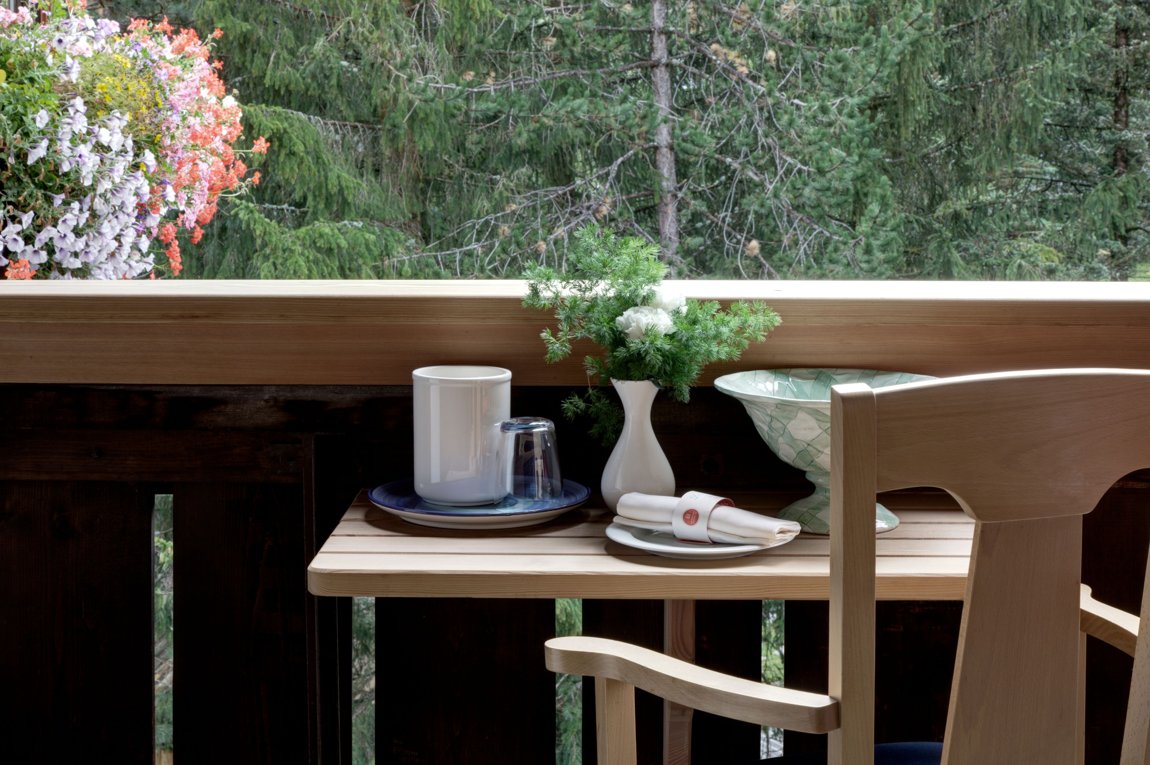 Une terrasse en bois avec une table dressée pour le repas, une chaise et un pot de fleurs.