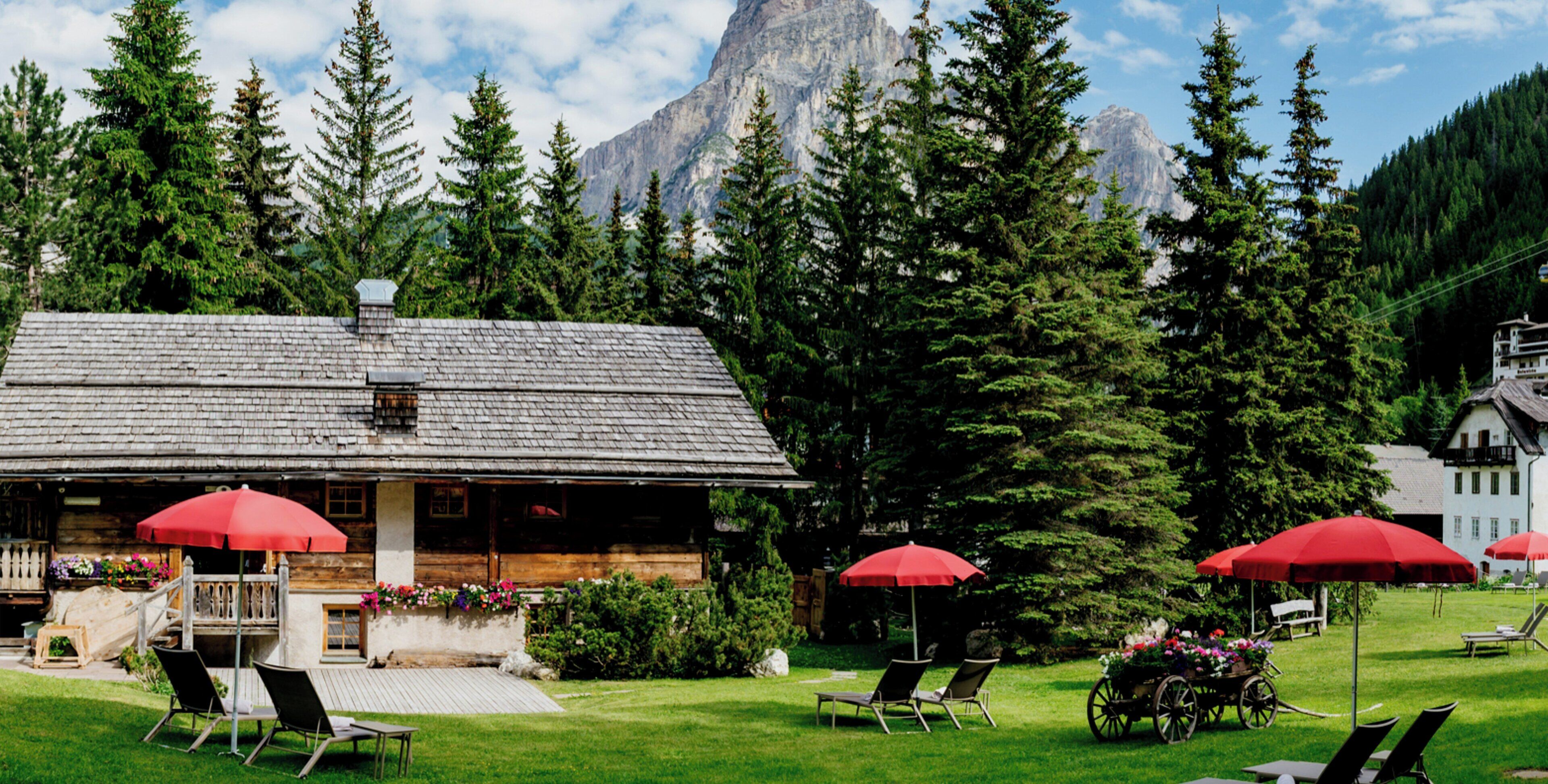 A lodge with a wooden exterior, outdoor seating with red umbrellas, and a mountain backdrop.