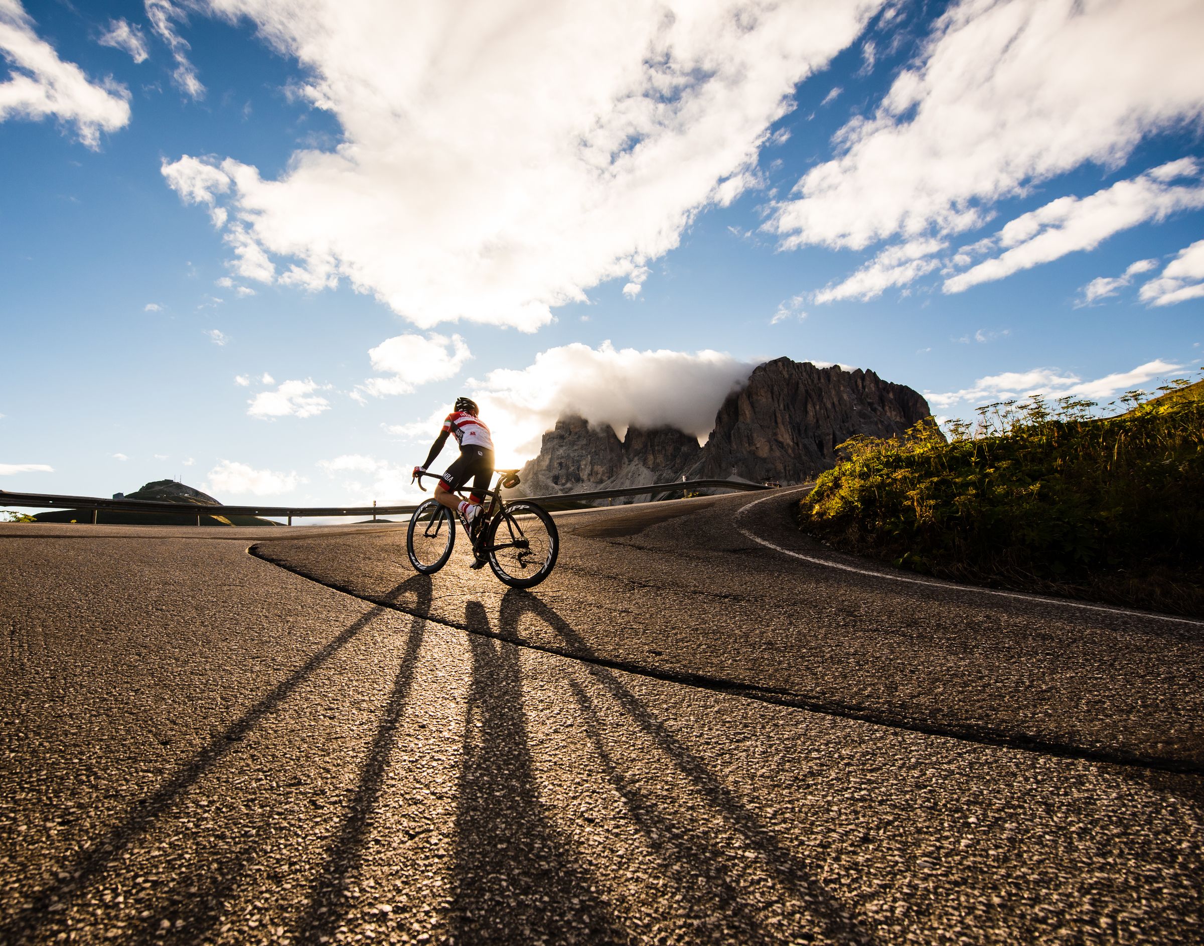 A cyclist on a paved road with a mountain in the background.