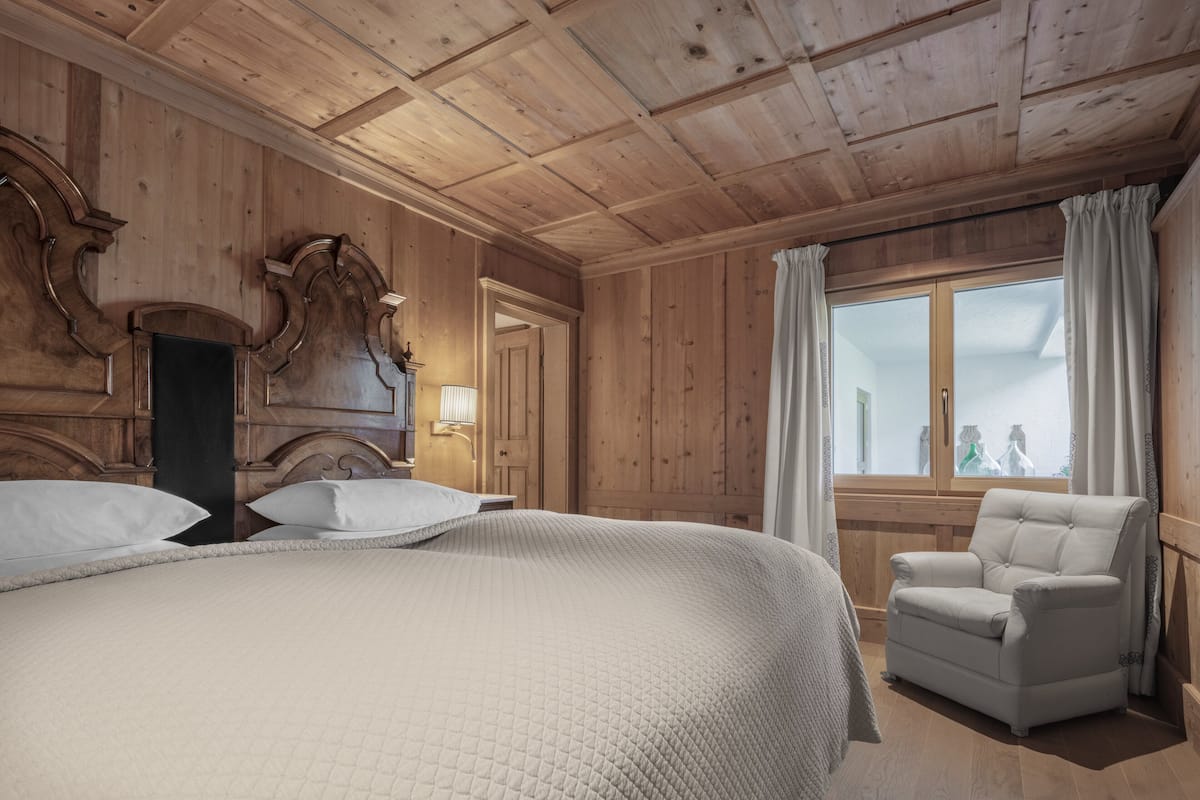 Een slaapkamer met houten lambrisering, een groot bed, een stoel en een raam met gordijnen.